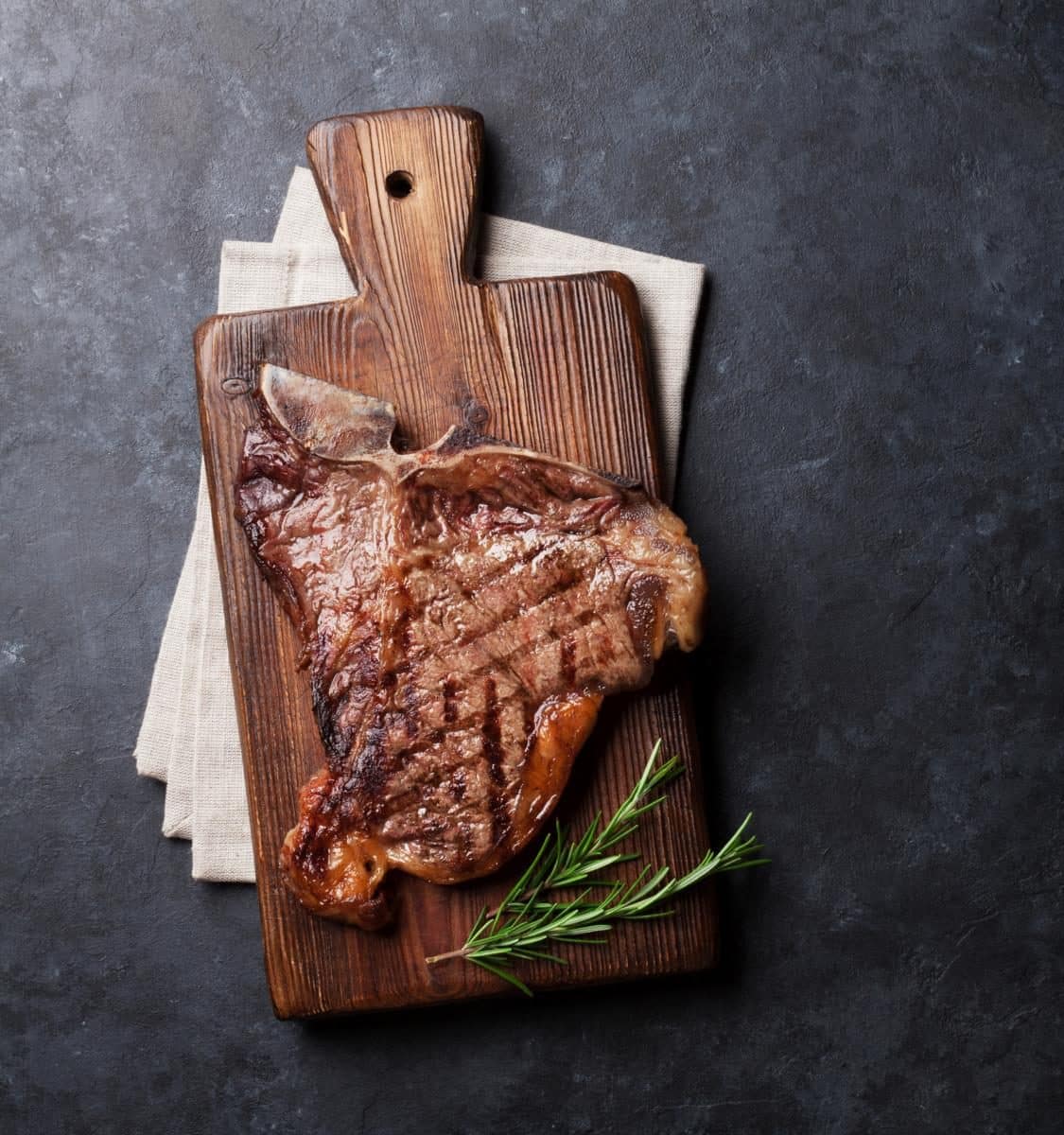 Grilled T-bone steak on stone table. Top view with copy space